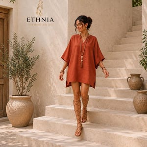 May include: A rust-colored tunic dress with a V-neckline and wide, elbow-length sleeves. The garment features side slits at the hem and is paired with a long beaded necklace, beaded bracelets, and brown lace-up gladiator sandals.