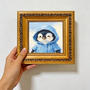 Peut inclure: Une peinture à l'huile carrée dans un cadre doré orné représentant un manchot portant un imperméable à capuche bleu. Le manchot a des plumes noires et blanches, un petit bec orange et les yeux fermés. Le fond est un ciel bleu clair nuageux.