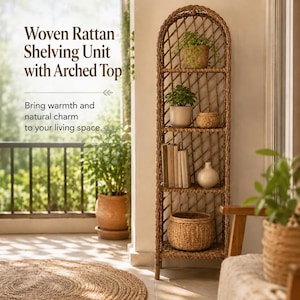 May include: A tall, light brown woven rattan shelving unit featuring an arched top and four horizontal shelves. The unit displays a potted green plant, a small woven basket, several upright books, a white ceramic vase, and a large woven basket.