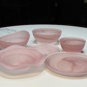 Puede incluir: Un conjunto de vajilla de vidrio translúcido en color rosa pálido con un patrón de remolinos marmolados. El set incluye un cuenco grande con bordes ondulados, un cuenco profundo, uno más pequeño y dos platos llanos, con acabado pulido.