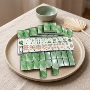 A jenga set made of green and white blocks is displayed on a plate, with a bowl and a fan in the background.