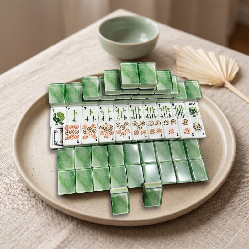 A jenga set made of green and white blocks is displayed on a plate, with a bowl and a fan in the background.