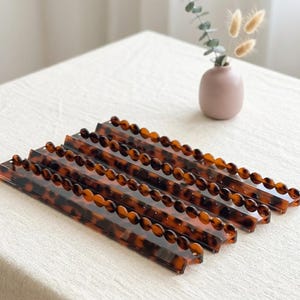 May include: A set of four rectangular acrylic organizers featuring a brown and black tortoiseshell pattern. Each organizer has a scalloped, rounded edge along the top length, creating a series of small, uniform semi-circular indentations.