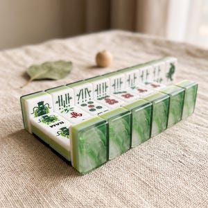 A set of green and white dominoes arranged on a beige surface, with a single leaf and a small wooden ball in the background.