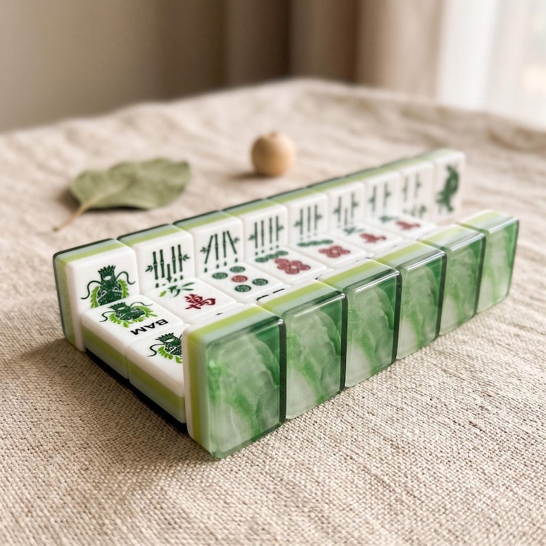 A set of green and white dominoes arranged on a beige surface, with a single leaf and a small wooden ball in the background.