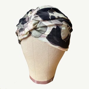 Peut inclure: Un bandeau turban avec un imprim&eacute; floral dans des tons de rose, noir et gris. Le bandeau est nou&eacute; sur le dessus de la t&ecirc;te.