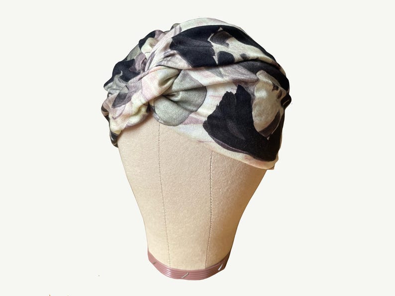 Peut inclure: Un bandeau turban avec un imprim&eacute; floral dans des tons de rose, noir et gris. Le bandeau est nou&eacute; sur le dessus de la t&ecirc;te.