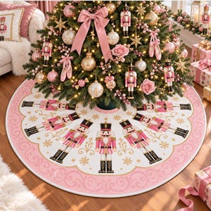 May include: A circular white Christmas tree skirt featuring a repeating pattern of pink and gold nutcracker figures arranged in a radial design. The border is decorated with a scalloped pink edge and gold filigree swirls, accented by small gold snowflakes.