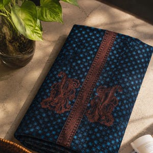 May include: A folded piece of dark blue fabric featuring a repeating pattern of small light blue stars. A central vertical band displays a brown geometric Greek key design, flanked by two large, intricate brown paisley-style motifs.