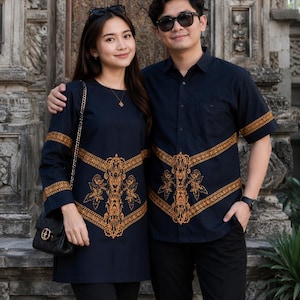 May include: A navy blue long-sleeved tunic and a matching navy blue short-sleeved button-down shirt, both featuring a prominent orange decorative pattern across the chest and sleeves, paired with black trousers and a black quilted shoulder bag.