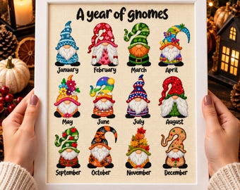 May include: A framed cross-stitch embroidery titled A year of gnomes, featuring twelve distinct gnomes representing each month of the year. Each gnome is decorated with seasonal motifs, including hearts, flowers, stars, pumpkins, and leaves, arranged in a grid with their corresponding month name printed below.