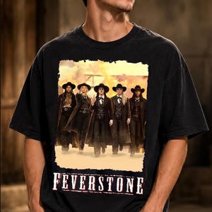 May include: A black short-sleeve t-shirt featuring a rectangular graphic print of five individuals wearing western-style hats, vests, and long coats. The text FEVERSTONE is printed in a white, distressed font below the central image.