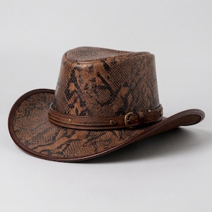 May include: A brown cowboy hat featuring a textured snakeskin pattern across the crown and brim. The hat includes a dark brown leather band around the base, accented with small metallic studs and a functional brass-toned buckle closure.