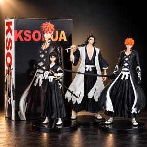 Puede incluir: Tres figuras de personajes de anime sobre bases circulares negras. Dos figuras tienen cabello naranja puntiagudo y visten trajes blancos y negros con espadas. La tercera figura tiene cabello negro, una capa blanca y una espada. Detrás hay una caja con KSOJA.