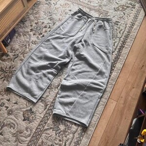 Peut inclure: Pantalon de jogging gris clair &agrave; jambes larges dot&eacute; d'une taille &eacute;lastique avec cordon de serrage, de deux grandes poches plaqu&eacute;es &agrave; l'avant et de coutures verticales sur le devant de chaque jambe. Le v&ecirc;tement est en tissu doux type molleton.