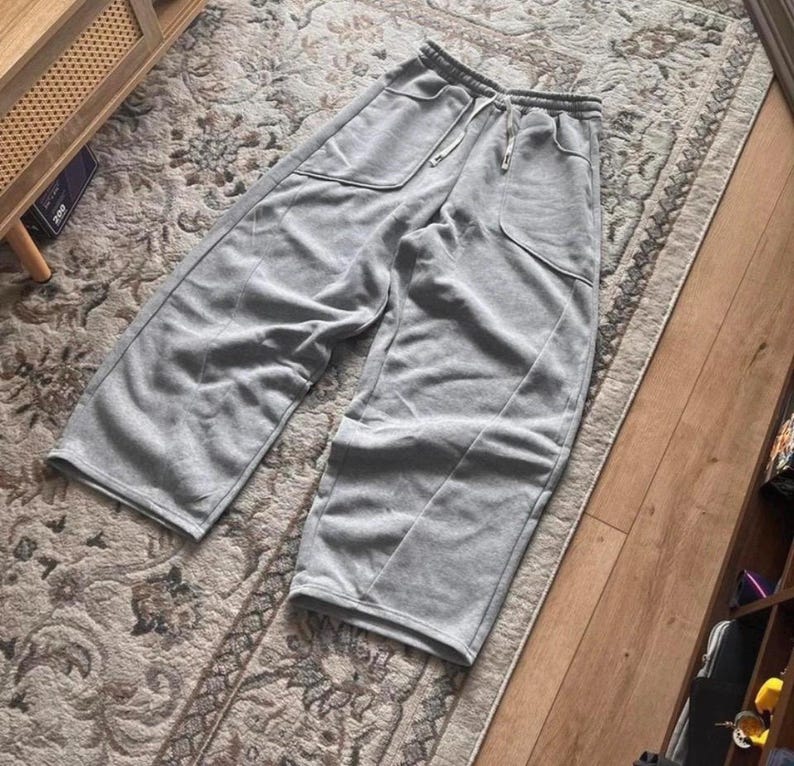 Peut inclure: Pantalon de jogging gris clair &agrave; jambes larges dot&eacute; d'une taille &eacute;lastique avec cordon de serrage, de deux grandes poches plaqu&eacute;es &agrave; l'avant et de coutures verticales sur le devant de chaque jambe. Le v&ecirc;tement est en tissu doux type molleton.