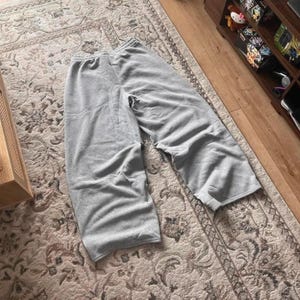 Peut inclure: Un pantalon de jogging gris clair dot&eacute; d'une coupe large, d'une taille &eacute;lastique et d'une allure d&eacute;contract&eacute;e. Le v&ecirc;tement est confectionn&eacute; dans un tissu chin&eacute; doux avec des coutures visibles le long du centre et des c&ocirc;t&eacute;s des jambes.