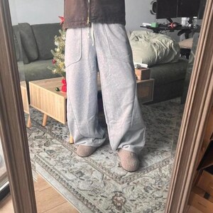 Peut inclure: Pantalon de jogging gris clair &agrave; jambes larges avec une taille &agrave; cordon de serrage, deux grandes poches plaqu&eacute;es &agrave; l'avant et des coutures verticales sur le devant de chaque jambe. Le pantalon est port&eacute; avec des chaussures beiges et une veste marron.