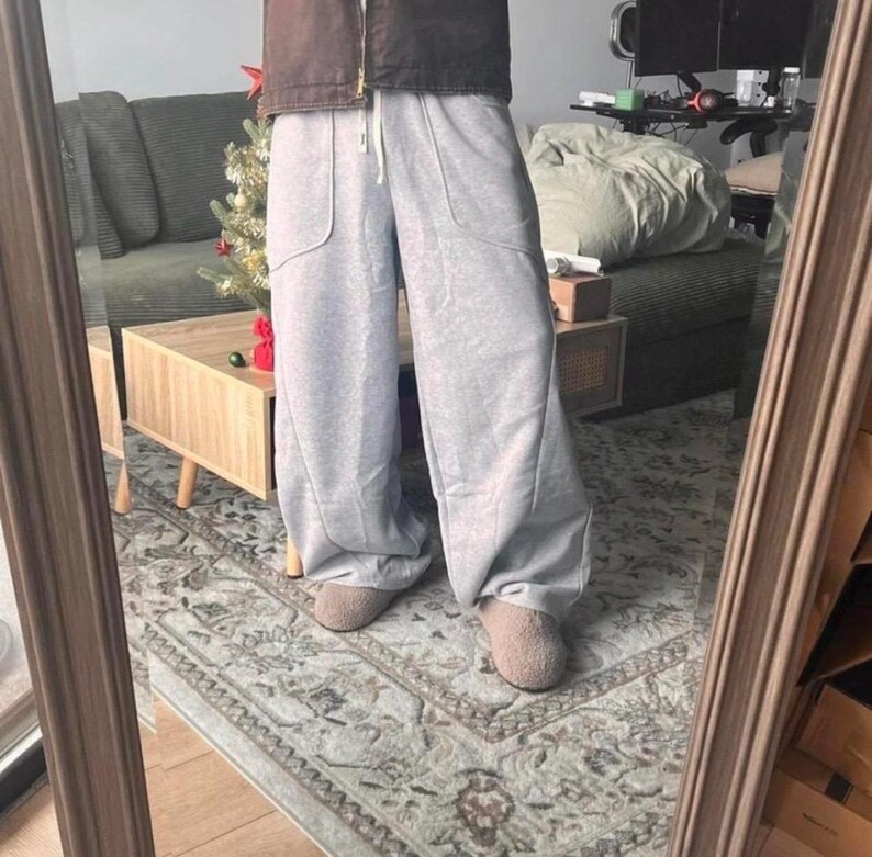 Peut inclure: Pantalon de jogging gris clair &agrave; jambes larges avec une taille &agrave; cordon de serrage, deux grandes poches plaqu&eacute;es &agrave; l'avant et des coutures verticales sur le devant de chaque jambe. Le pantalon est port&eacute; avec des chaussures beiges et une veste marron.