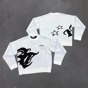 Könnte beinhalten: Ein weißer Langarmpullover mit Rundhalsausschnitt und einem großen schwarzen Grafikdesign auf Vorder- und Rückseite. Auf der Vorderseite steht das Wort Amici in Schreibschrift. Die Rückseite zeigt zwei schwarze Sternumrisse und ein Teilmuster.