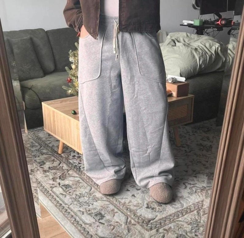 Peut inclure: Pantalon de jogging gris clair &agrave; coupe large, dot&eacute; d'une taille haute &eacute;lastique avec un cordon de serrage blanc et de deux grandes poches plaqu&eacute;es sur le devant. Le pantalon est associ&eacute; &agrave; des chaussons duveteux beiges et une veste marron.