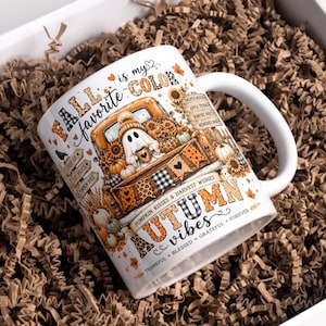 May include: A white ceramic mug featuring a colorful autumn-themed graphic. The design includes a ghost sitting in an orange truck bed filled with sunflowers and pumpkins, with text reading "FALL is my favorite COLOR" and "AUTUMN vibes".