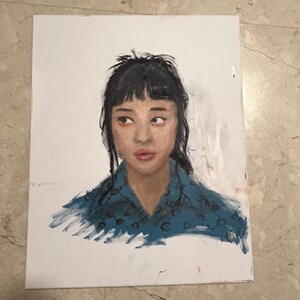 Puede incluir: Una pintura al óleo sobre un lienzo rectangular que representa el retrato de una persona con cabello oscuro y flequillo, vistiendo una camisa de cuello azul con un patrón circular oscuro. El sujeto mira hacia la izquierda sobre un fondo blanco.