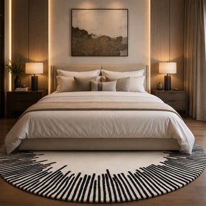 Può includere: Una camera da letto con un grande letto con biancheria bianca e diversi cuscini beige, affiancato da due comodini in legno scuro con lampade. Un tappeto rotondo con un motivo a linee radiali bianche e nere si trova sul pavimento.