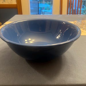 Puede incluir: Un cuenco de cerámica de color azul marino profundo y sólido con un acabado liso y brillante. El cuenco presenta un borde circular ancho y abierto y una base redondeada, mostrando un diseño simple y funcional con reflejos visibles.