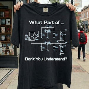 Op de afbeelding: Een zwart t-shirt met korte mouwen en een witte afbeelding van een elektronisch schakelschema. De tekst "What Part of..." staat boven het diagram en "Don't You Understand?" staat in een vetgedrukt wit lettertype onder het diagram.