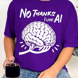 Könnte beinhalten: Ein violettes T-Shirt mit einer weißen Grafik eines menschlichen Gehirns, das von einer Gabel angehoben wird. Über dem Gehirn steht der Text "NO THANKS I USE AI" in einer fetten, weißen, handgezeichneten Schriftart, zentriert auf der Brust.