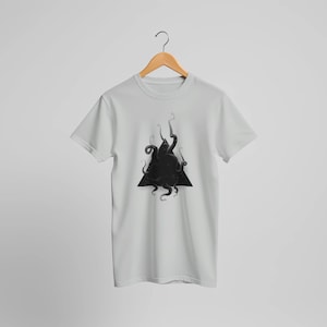 May include: A light grey short-sleeved t-shirt featuring a central graphic of a black triangle filled with dark, swirling tentacles. The garment is displayed on a wooden hanger, showcasing a crew neckline and a standard straight-cut hemline.