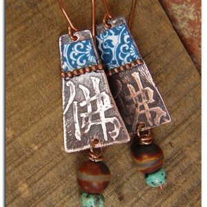 May include: Copper earrings with blue and white patterned metal accents, brown and turquoise beads, and the Chinese character for "peace" embossed on the metal.