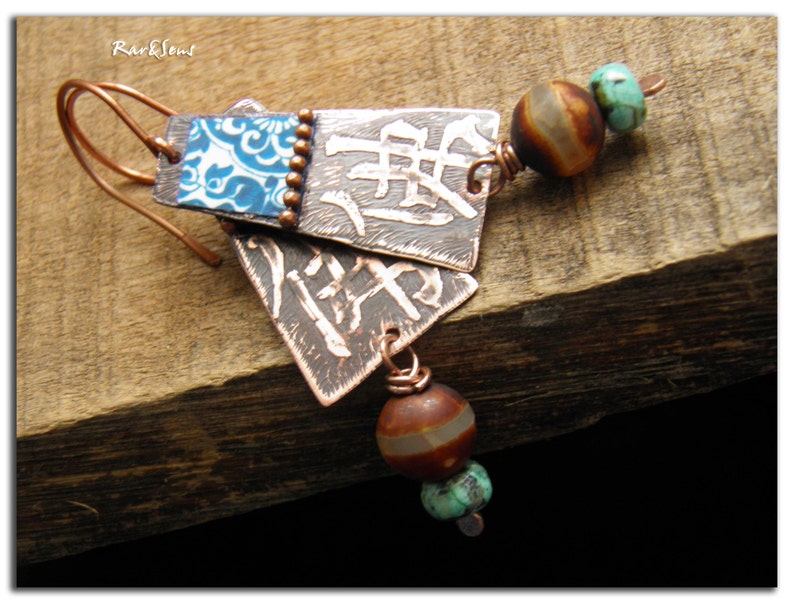 May include: Copper earrings with blue and white patterned tiles, brown and white agate beads, and turquoise beads. The earrings are hanging from a wooden surface.