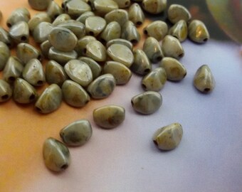 May include: A pile of light green and brown oval-shaped beads with a mottled pattern. The beads have a hole through the centre for stringing.