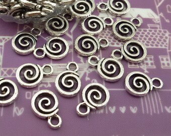 Puede incluir: Primer plano de un montón de abalorios de metal plateado en forma de espiral. Los abalorios tienen un bucle en la parte superior para sujetarlos a joyas u otras manualidades.