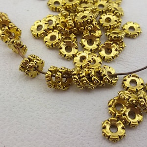 Peut inclure: Un grand nombre de perles en métal de couleur dorée avec un motif décoratif. Les perles sont enfilées sur un fil fin.