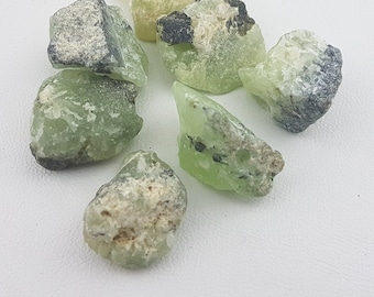 Puede incluir: Una colección de siete piedras preciosas en bruto de color verde y negro. Las piedras son de varias formas y tamaños.