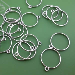 May include: A group of silver metal circle pendant blanks with a jump ring attached to each blank.