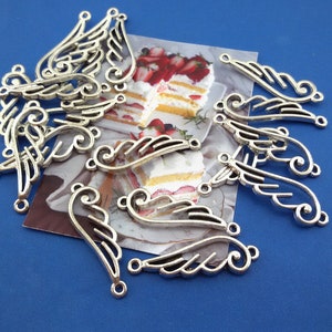 May include: A set of ten silver-toned metal angel wing charms. The wings are detailed with intricate scrollwork and have two jump rings for attaching to jewellery or other crafts.