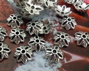 May include: A collection of silver metal flower-shaped bead caps. The caps have a delicate, intricate design and are perfect for adding a touch of elegance to jewelry projects.