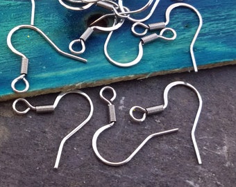 May include: A close-up of a pile of silver-toned earring hooks. The hooks are made of metal and have a spring-loaded closure. The hooks are arranged in a random pattern on a blue surface.