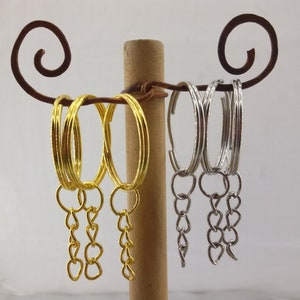 May include: Three gold keyrings with heart-shaped links and three silver keyrings with heart-shaped links hanging from a wooden stand.