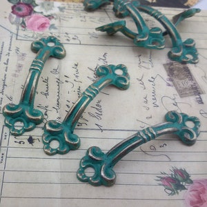 May include: Six antique-style drawer pulls with a teal green finish and ornate details. The pulls are made of metal and have a slightly distressed look.