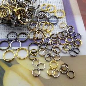 Puede incluir: Un gran surtido de anillas de salto en plata, oro y bronce. Las anillas son de varios tamaños y están esparcidas sobre una superficie blanca.