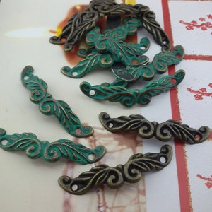 Könnte beinhalten: Eine Sammlung von verzierten Metallelementen mit einer grünen Patina. Die Elemente sind in Form von Blättern und Spiralen gestaltet und haben zwei Löcher zum Befestigen an einem Projekt.