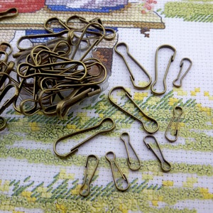 Può includere: Un mucchio di portachiavi o anelli di salto in metallo dorato. Gli anelli sono di varie dimensioni e forme, alcuni sono aperti e altri sono chiusi. Gli anelli sono su un tessuto a motivi bianchi e verdi.