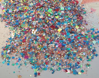 May include: A pile of iridescent glitter in various shades of blue, red, and gold. The glitter is made up of small squares and circles.