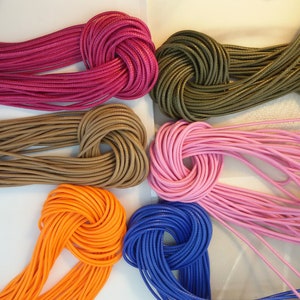 May include: Assortment of colourful cords in various colours, including pink, orange, blue, brown, green, and red. The cords are arranged in a circle and tied in a knot.
