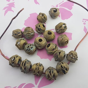 May include: A collection of 18 gold-toned metal beads with a wire mesh design. The beads are arranged in a circle on a pink background.